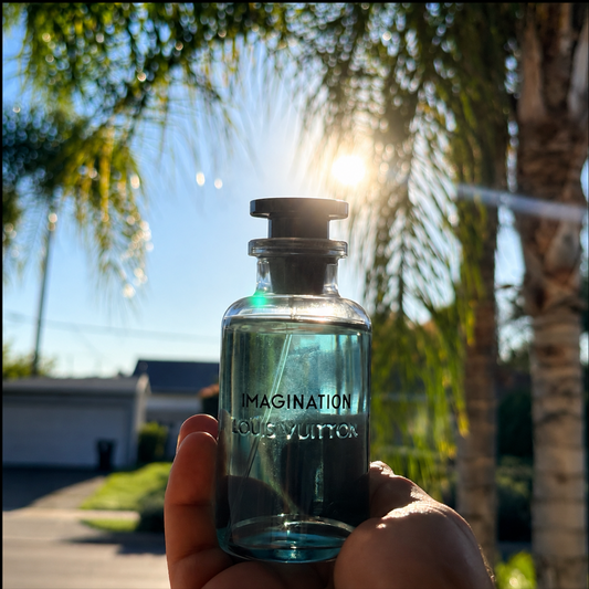 Person holding a 'Imagination' perfume bottle of Louis Vuitton with palm trees in the background
